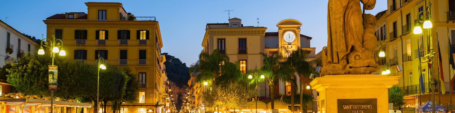 A bustling square with a statue, historic buildings, and a clock tower.