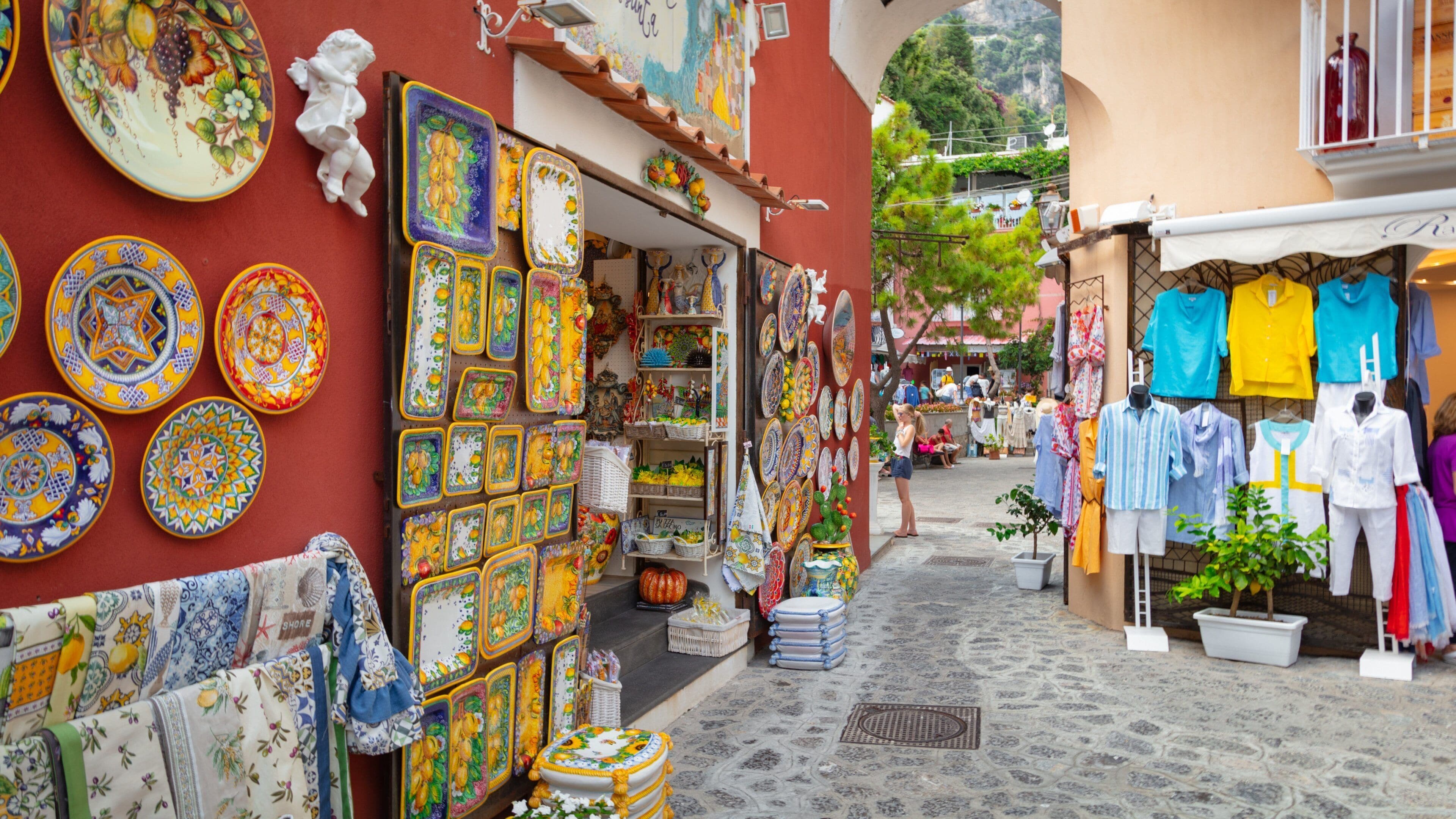 Uma rua estreita com cerâmicas e tecidos coloridos expostos em lojas.