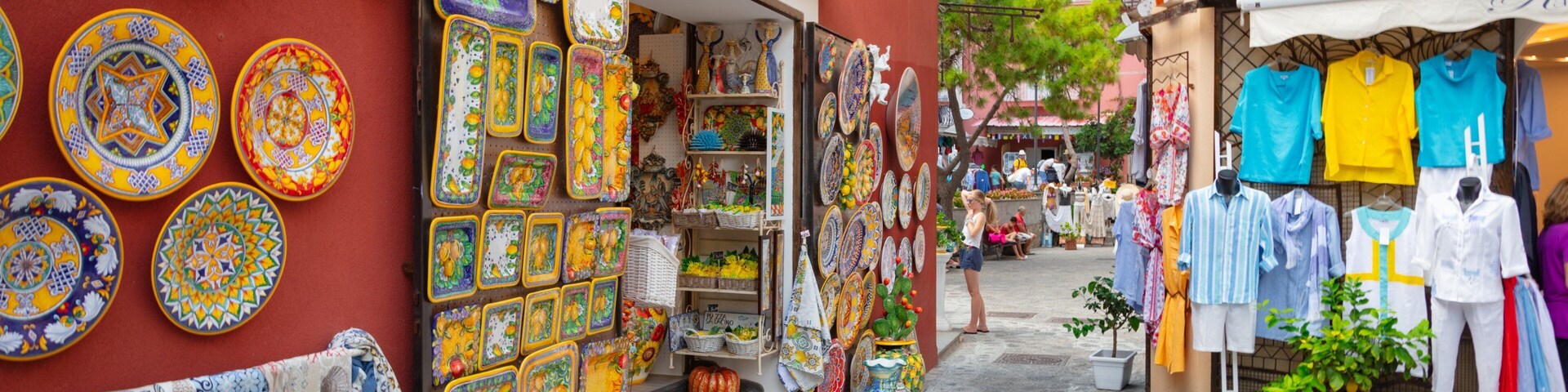 Uma rua estreita com cerâmicas e tecidos coloridos expostos em lojas.
