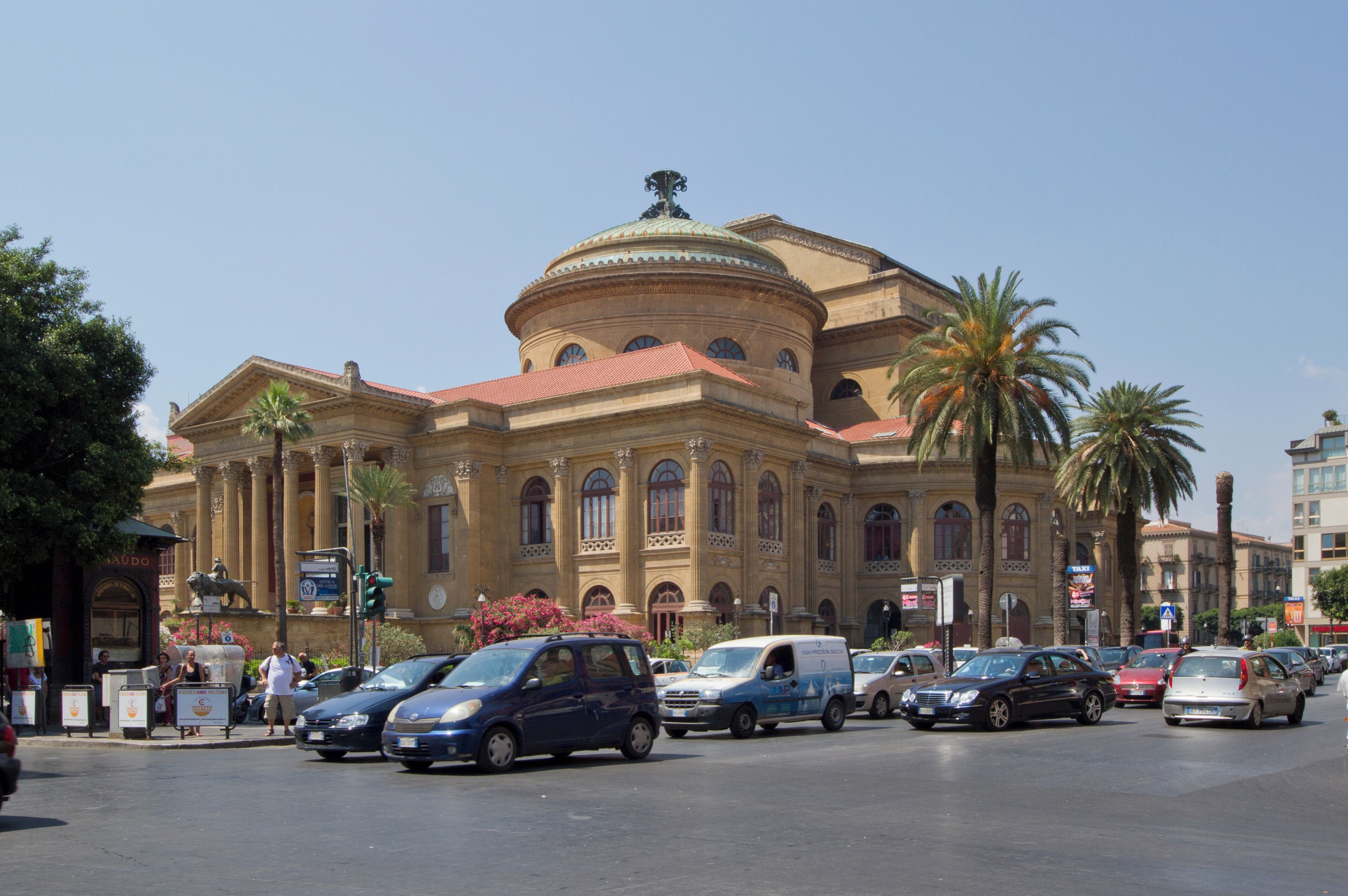A historic building with a dome and columns, surrounded by palm trees and busy streets with cars.