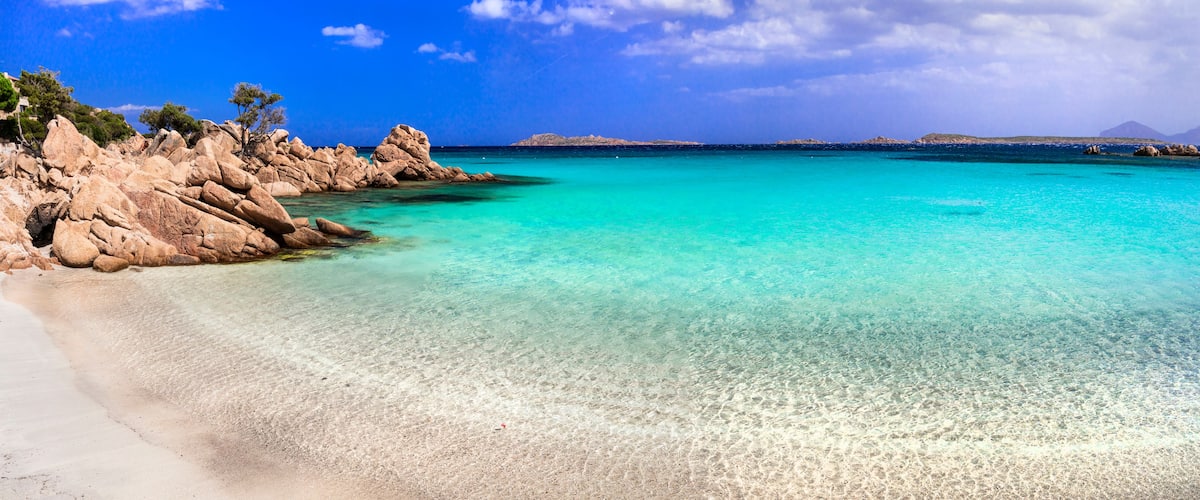 A clear turquoise sea, rocky coastline, and distant mountains.