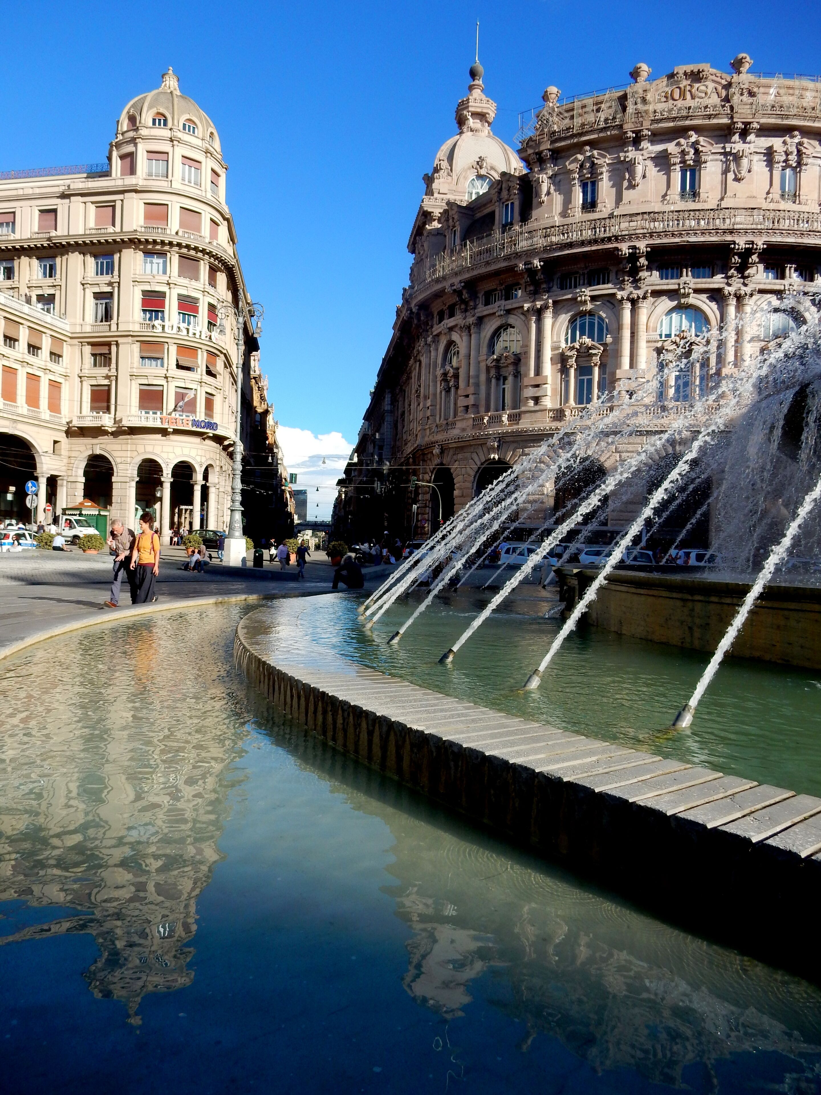 A historic fountain with water jets in a plaza, surrounded by ornate buildings.