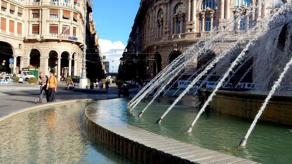A historic fountain with water jets in a plaza, surrounded by ornate buildings.