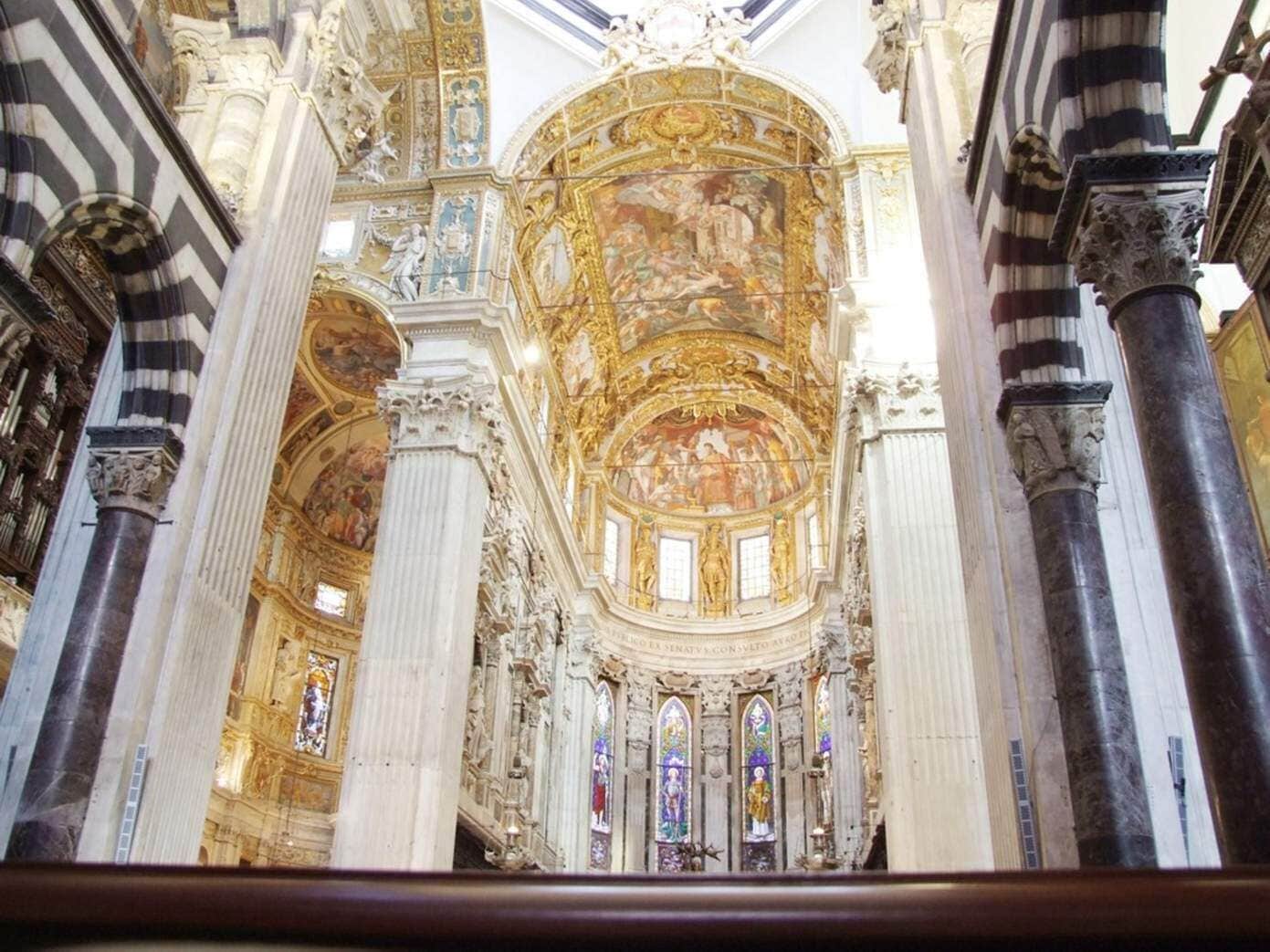 An ornate church interior with high ceilings, detailed frescoes, and stained glass windows.