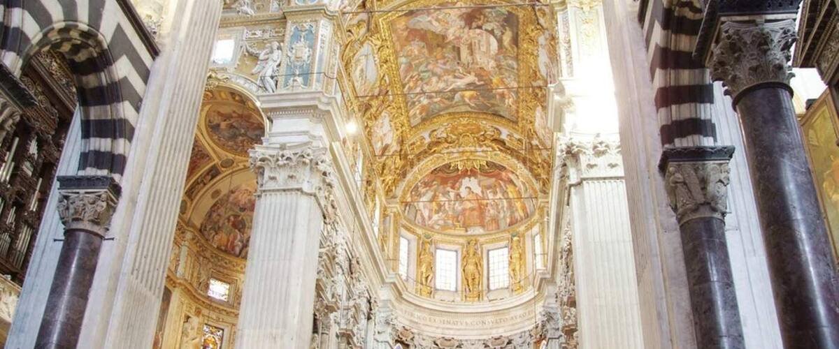 An ornate church interior with high ceilings, detailed frescoes, and stained glass windows.