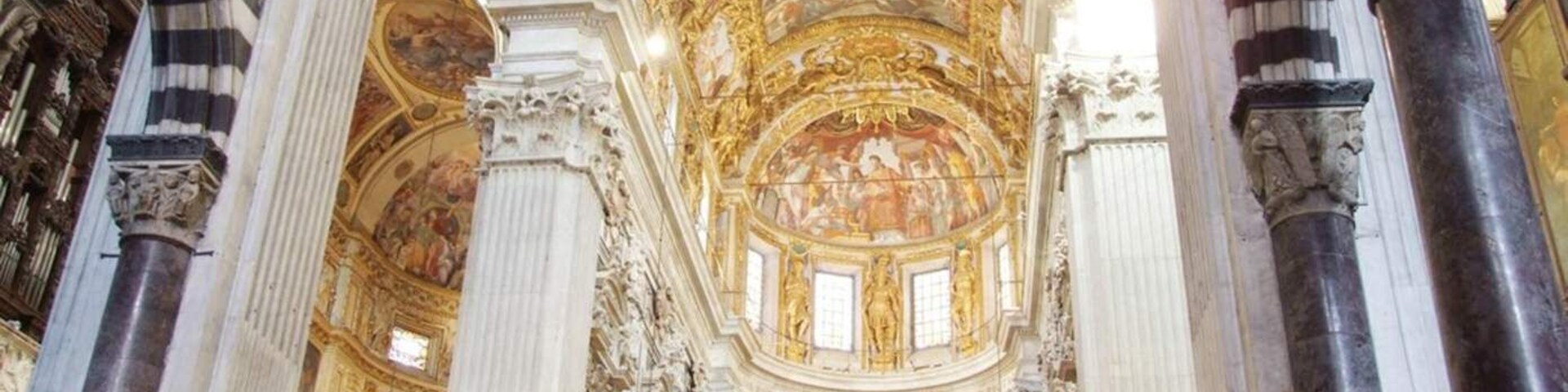 An ornate church interior with high ceilings, detailed frescoes, and stained glass windows.