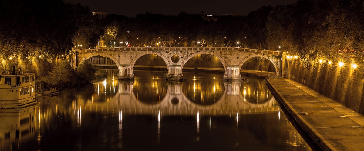 Un puente de piedra de noche, con luces que se reflejan en el agua.