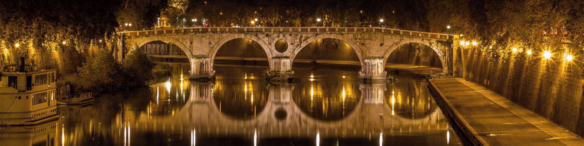 A stone bridge at night with lights reflecting on the water.