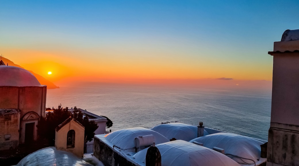 Panoramic view on church Chiesa Nuova during sunrise. Golden hour in coastal town Positano, Amalfi Coast, Italy, Campania, Europe. Vacation at coastline at the Mediterranean Sea. Praiano in distance