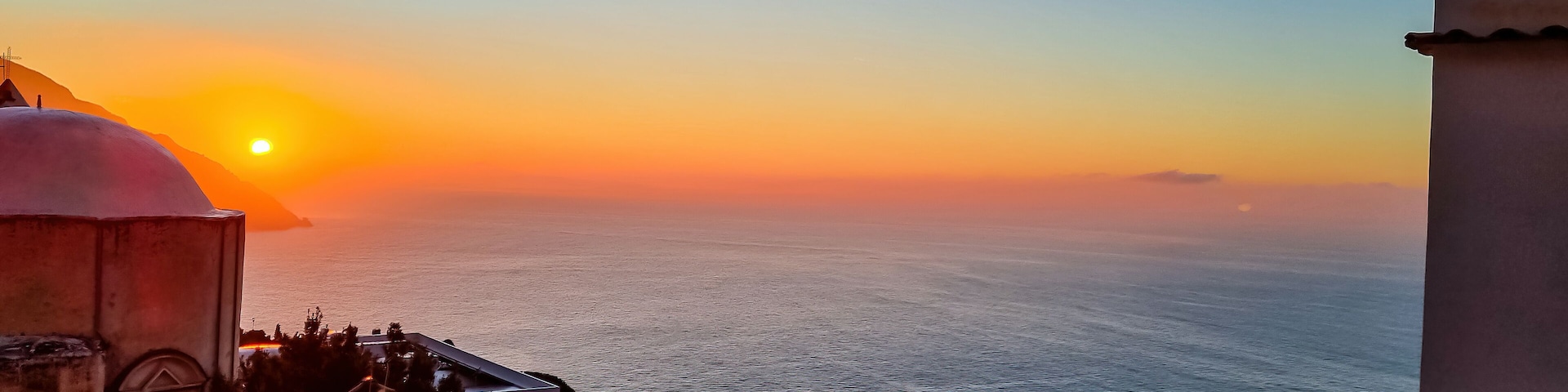 Panoramic view on church Chiesa Nuova during sunrise. Golden hour in coastal town Positano, Amalfi Coast, Italy, Campania, Europe. Vacation at coastline at the Mediterranean Sea. Praiano in distance