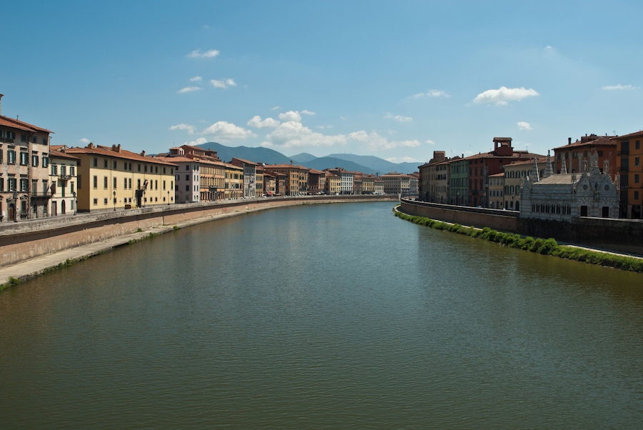 Un río bordeado por edificios históricos y montañas al fondo.