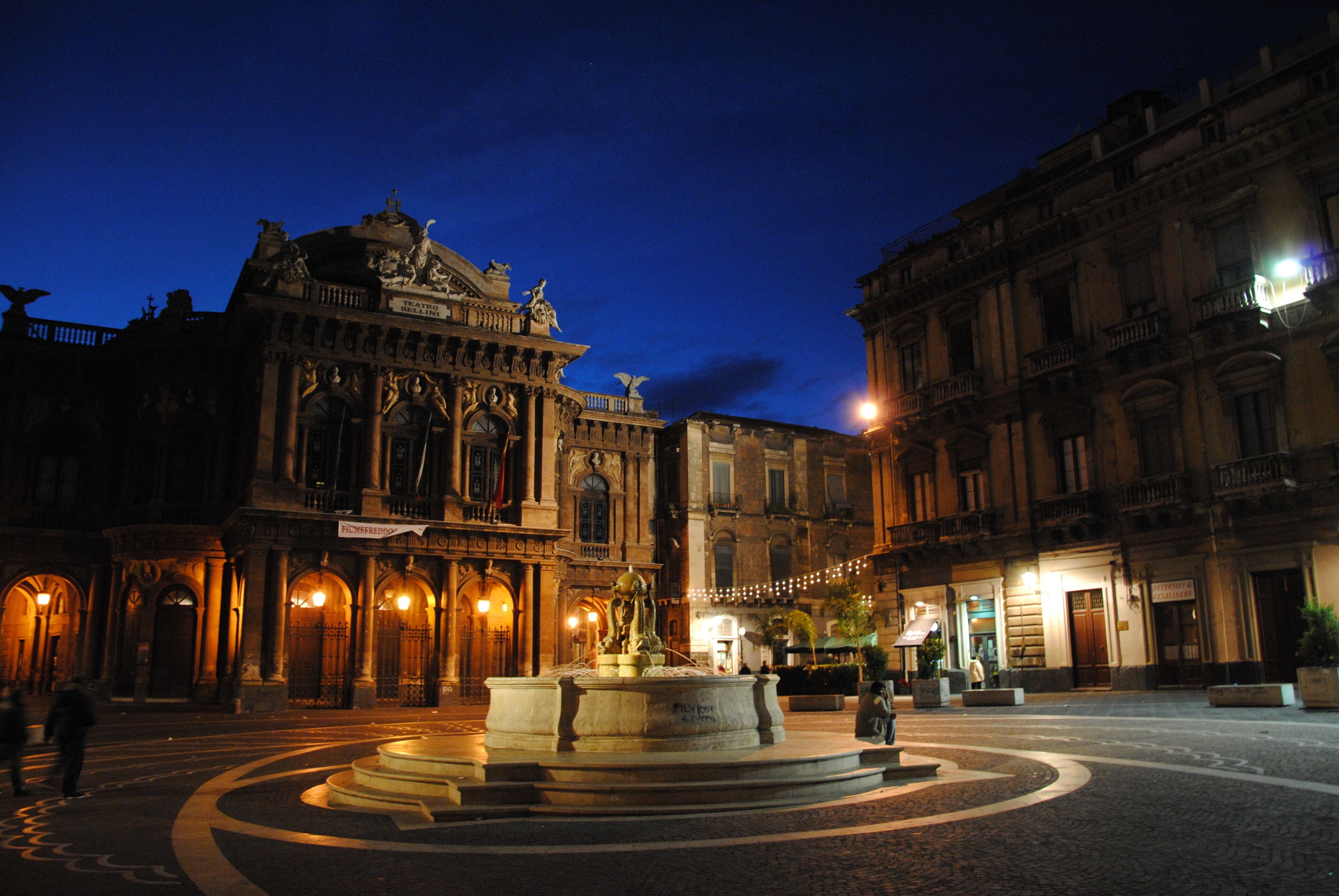 Une place historique, ornée de bâtiments élégants et dotée d’une fontaine centrale, au crépuscule.
