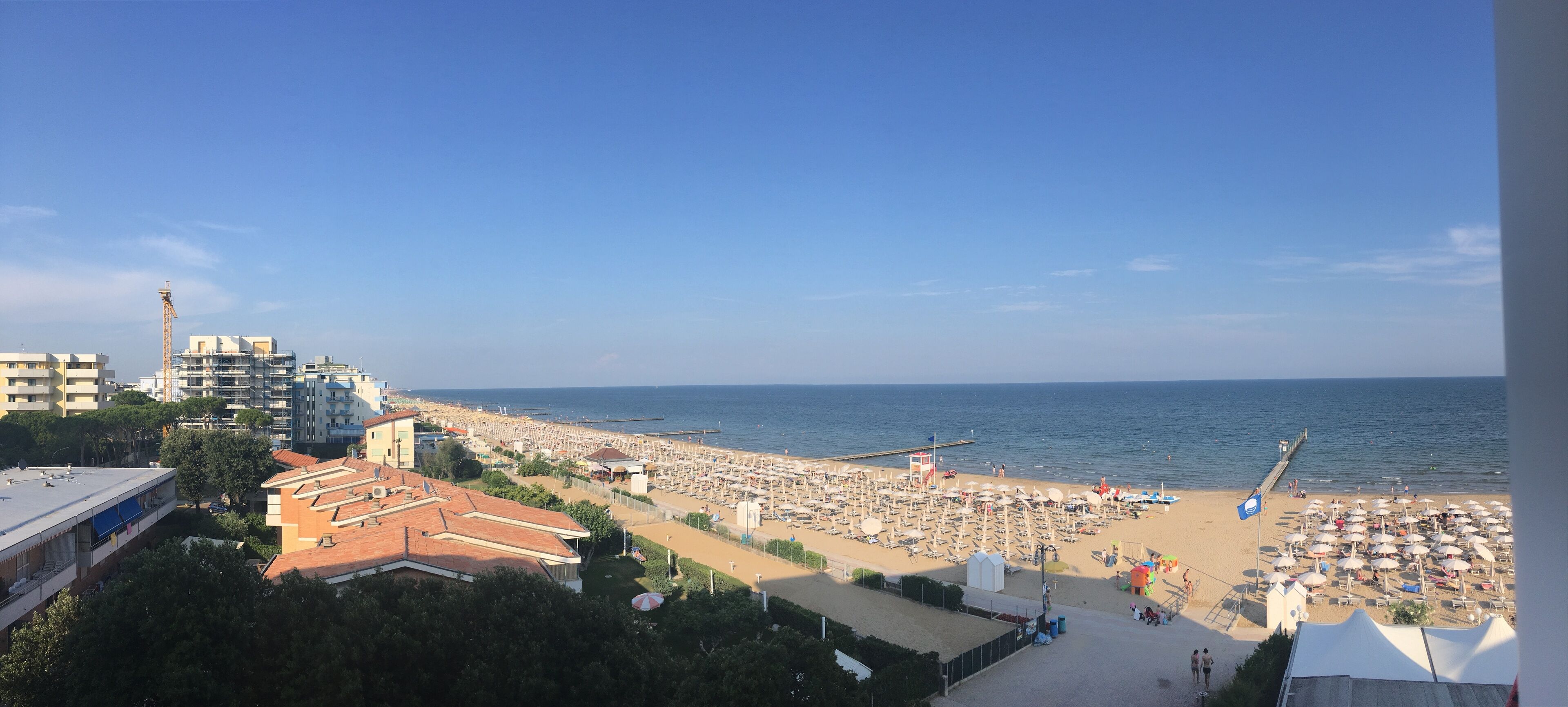 A beach with umbrellas and sun loungers, a pier extending into the water, and buildings in the background.