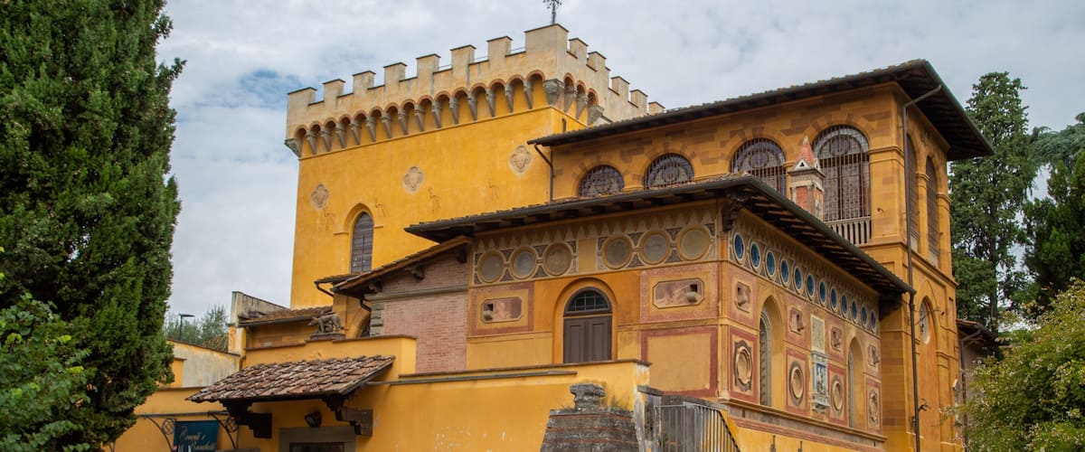 A historic yellow building with a tower, arched windows, and a stone staircase.