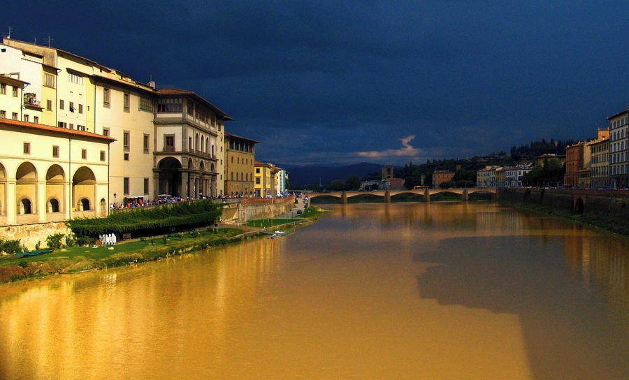 A river with a bridge, buildings, and a crowd of people.