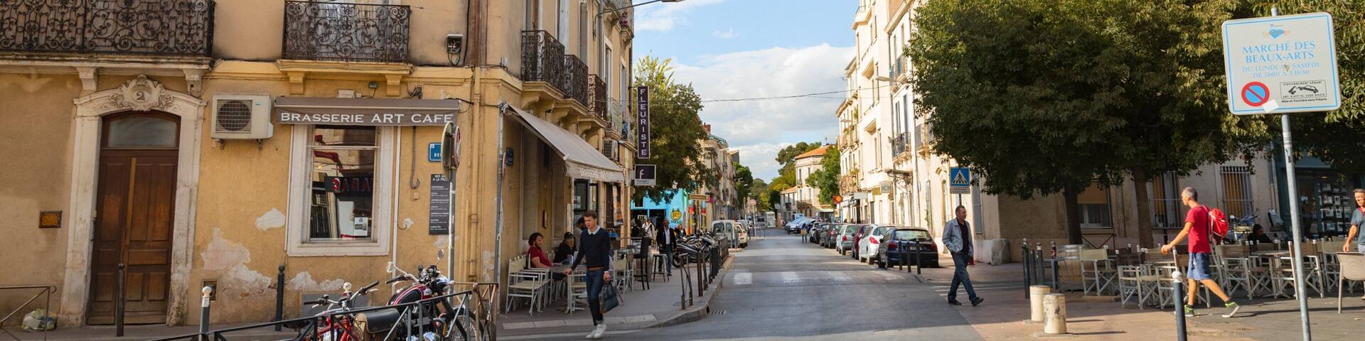 A street with buildings, a café, parked bicycles, and a pedestrian crossing sign.