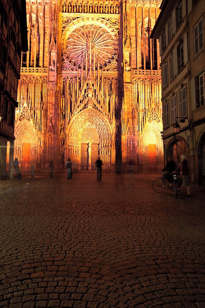 A cathedral with intricate Gothic architecture, a large rose window, and cobblestone pavement.