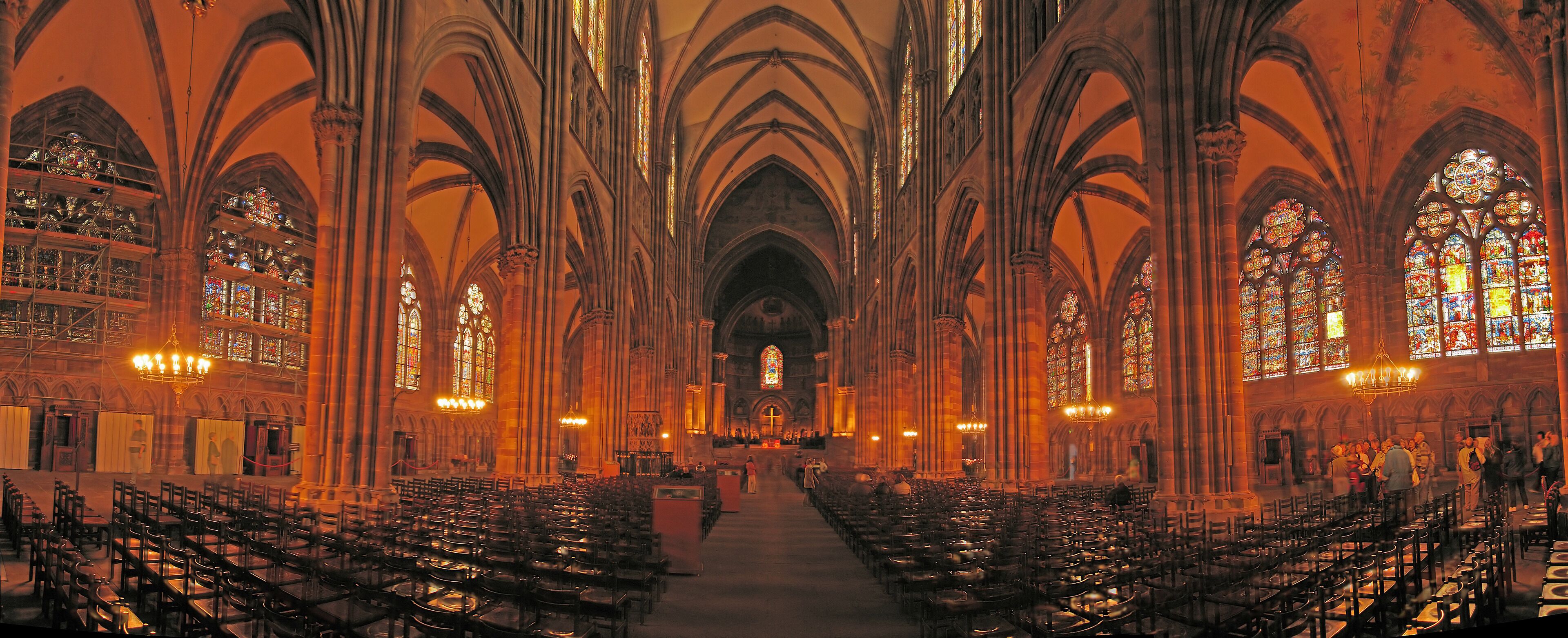 L’intérieur d’une cathédrale, avec de hauts plafonds en voûte, des vitraux et des rangées de bancs.