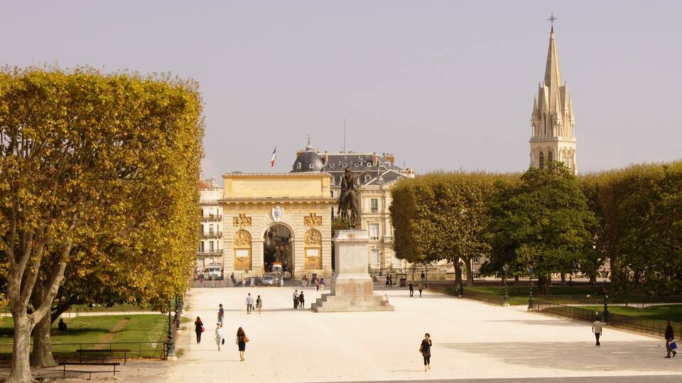 Une vaste place dégagée, ornée d’une statue, un grand bâtiment surmonté d’un dôme et un clocher d’église imposant.