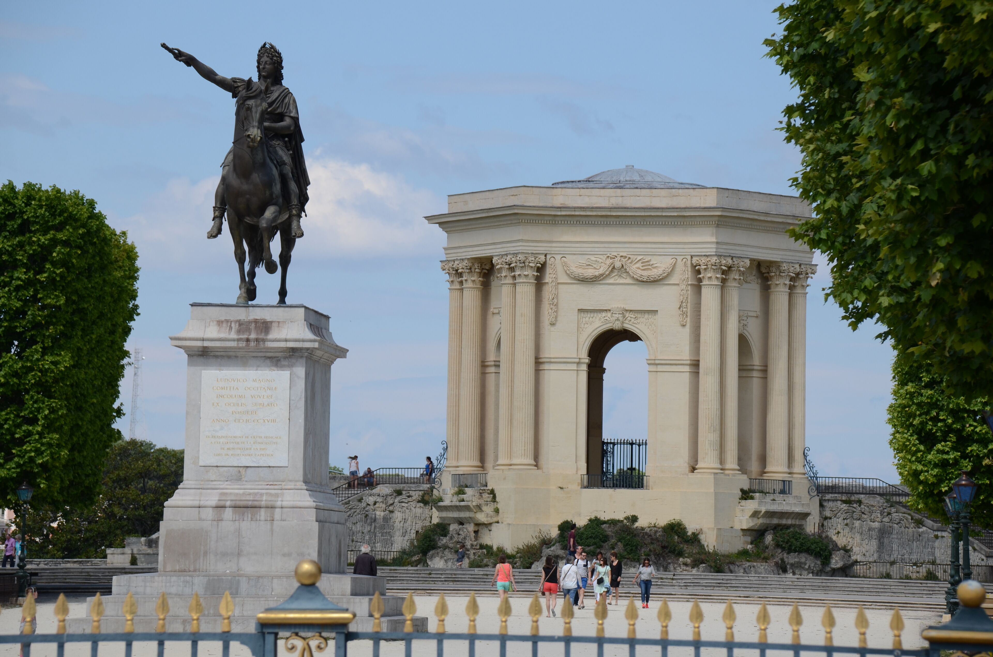 A statue of a man on horseback, a large archway, and people walking around.