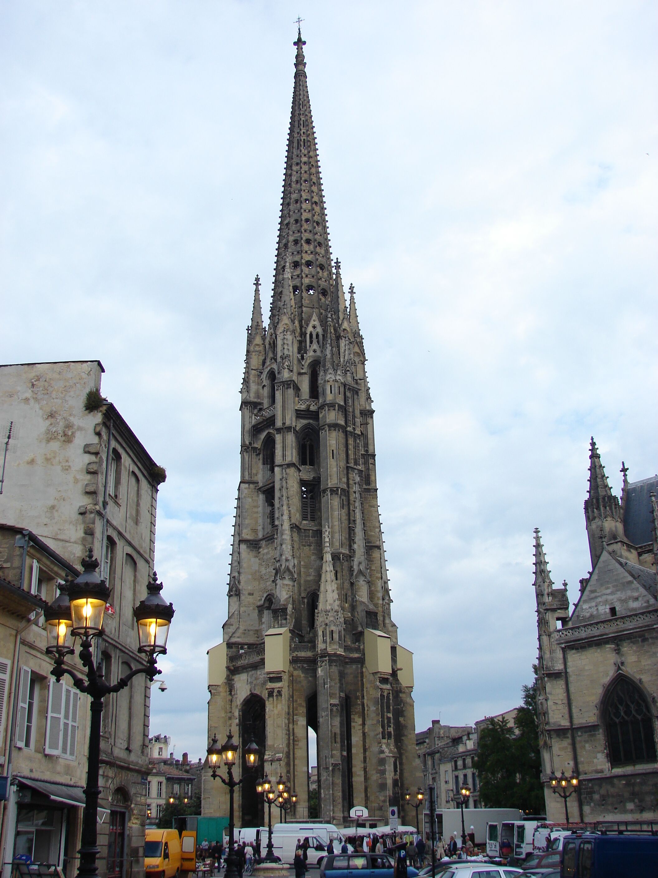 A Gothic cathedral with a tall spire, surrounded by historic buildings and street lamps.