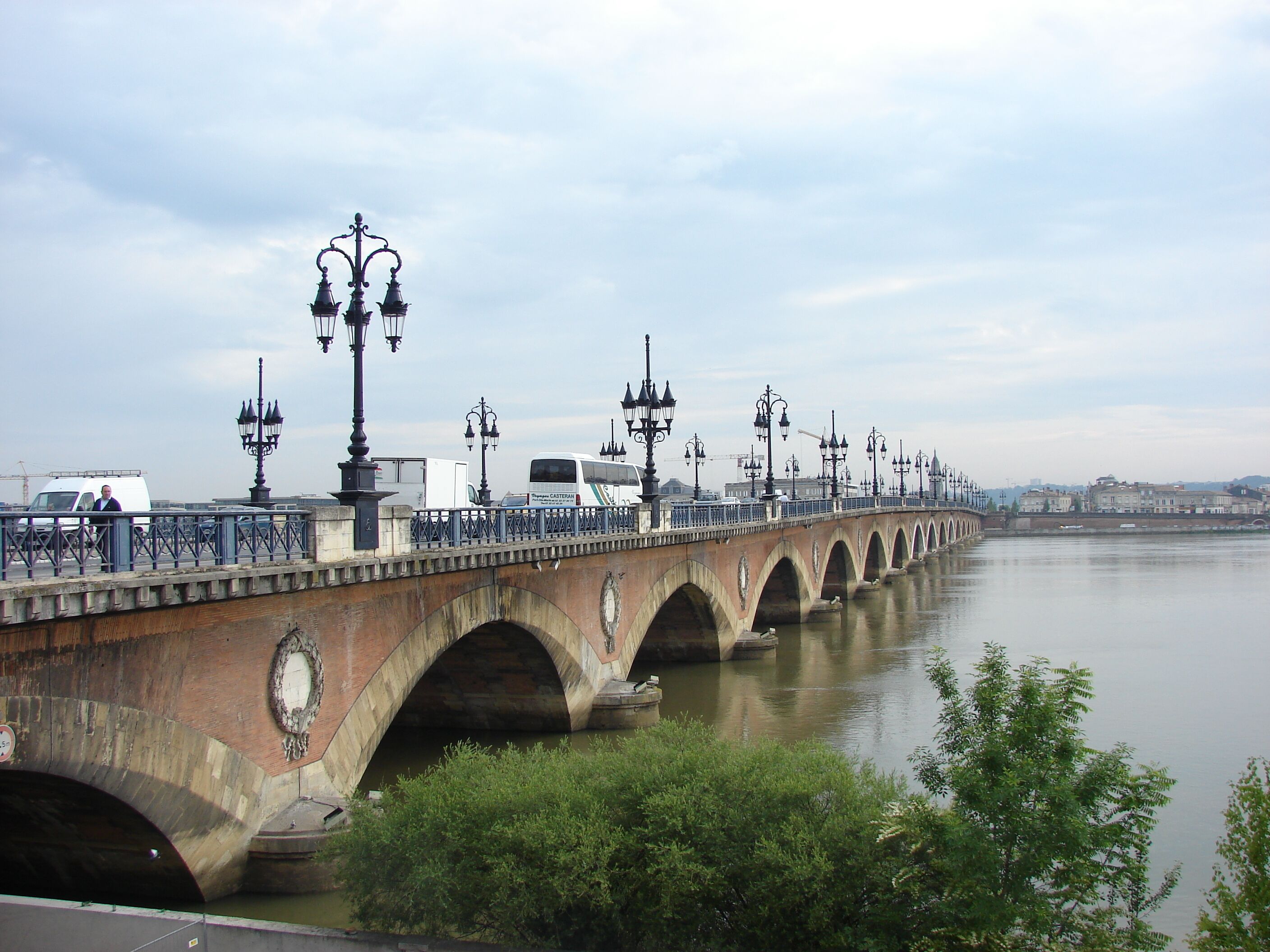 Un pont en pierre, doté de plusieurs arches, enjambe une rivière et est bordé de lampadaires et d’une rambarde.