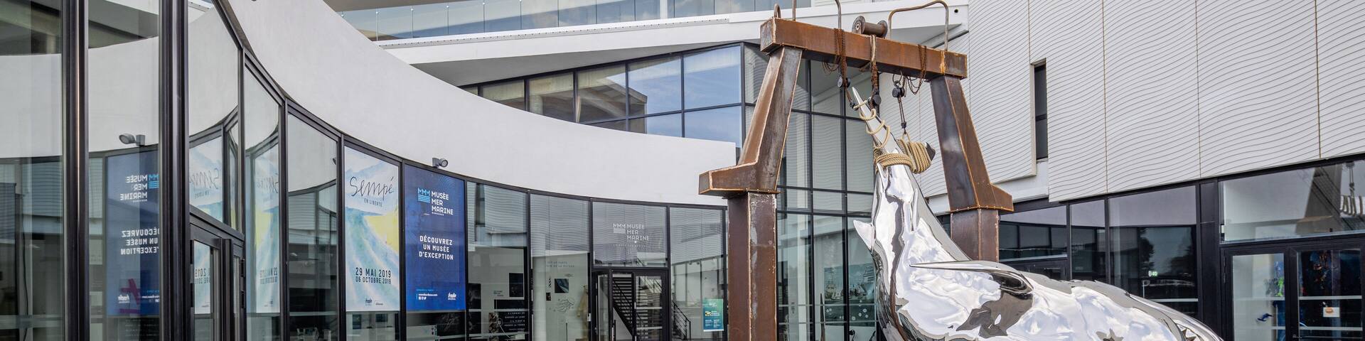 A modern building with glass windows and a large metallic sculpture of a bird.