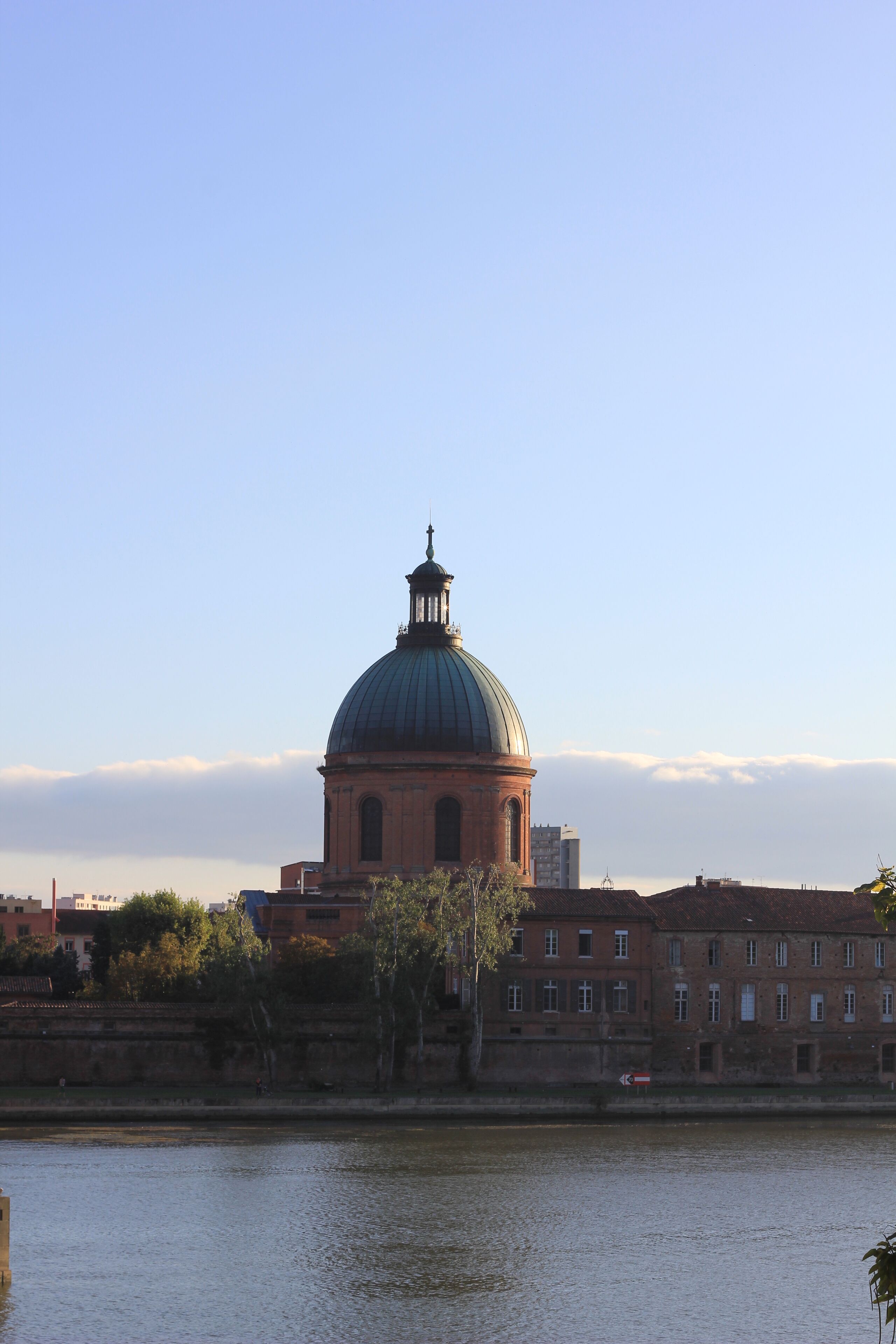 A domed building with a clock tower, a river, and a bridge in the foreground.