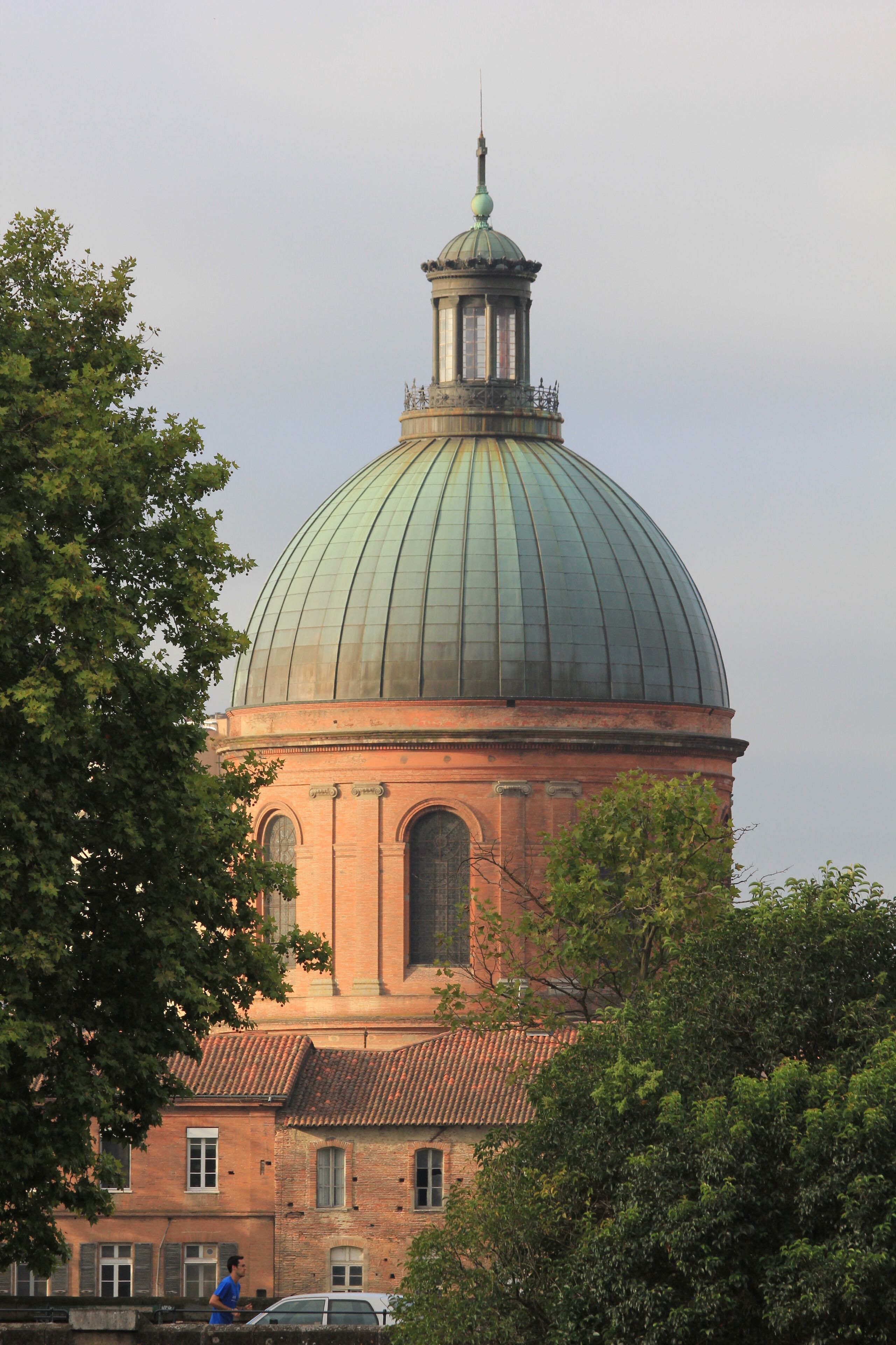 A large domed building with a greenish dome and a spire, surrounded by trees.