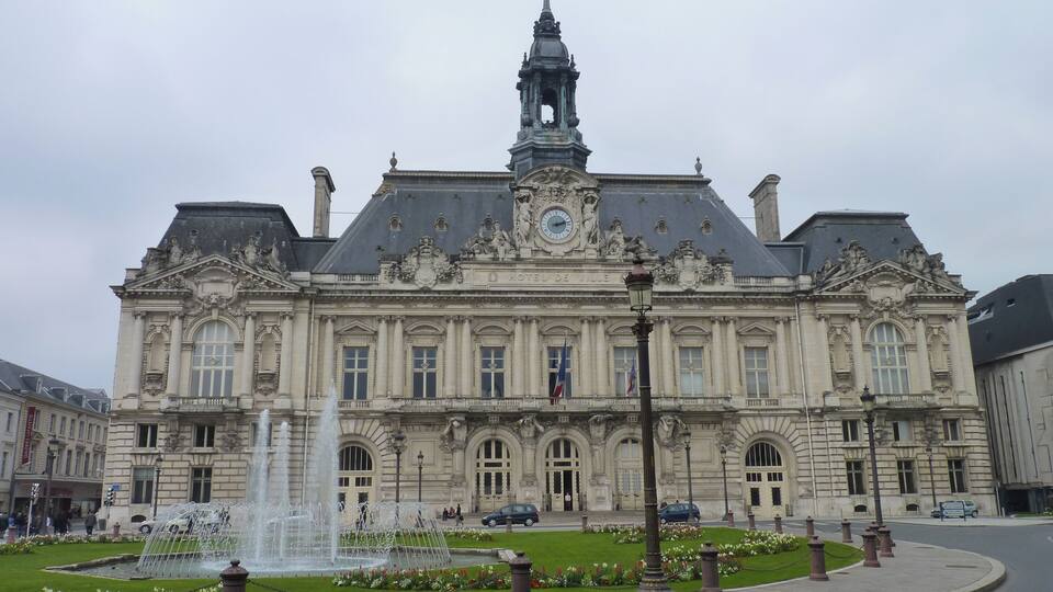 Un grand bâtiment historique doté d’un imposant clocher et d’une fontaine à l’avant.