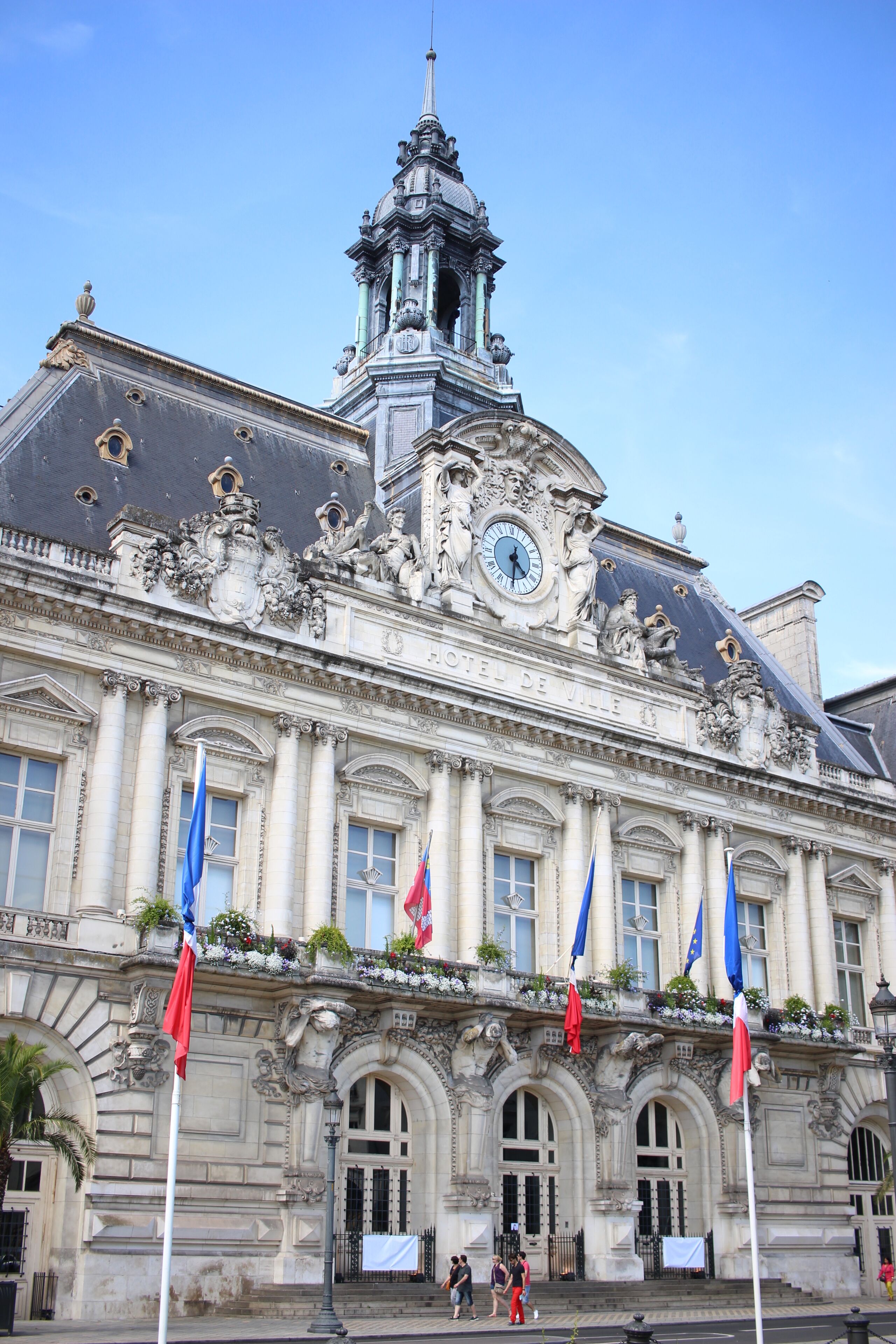 Un bâtiment historique à l’architecture riche et élaborée, doté d’un imposant clocher et de nombreux drapeaux.