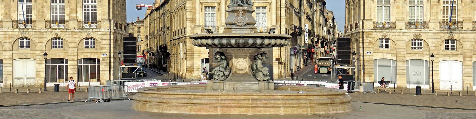 A historic square with a central fountain, flanked by grand buildings with classical architecture.