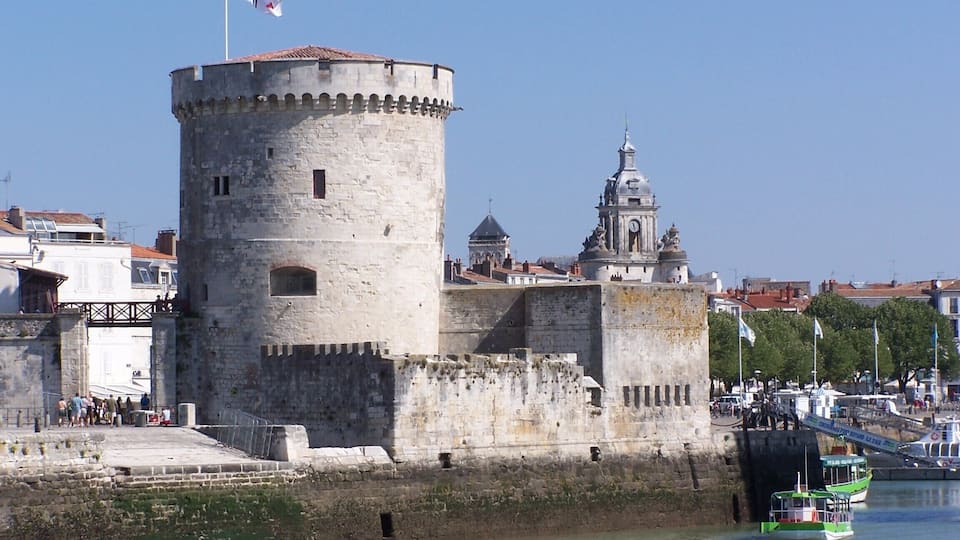 A historic tower with a flag, a church with a dome, and a river with boats.