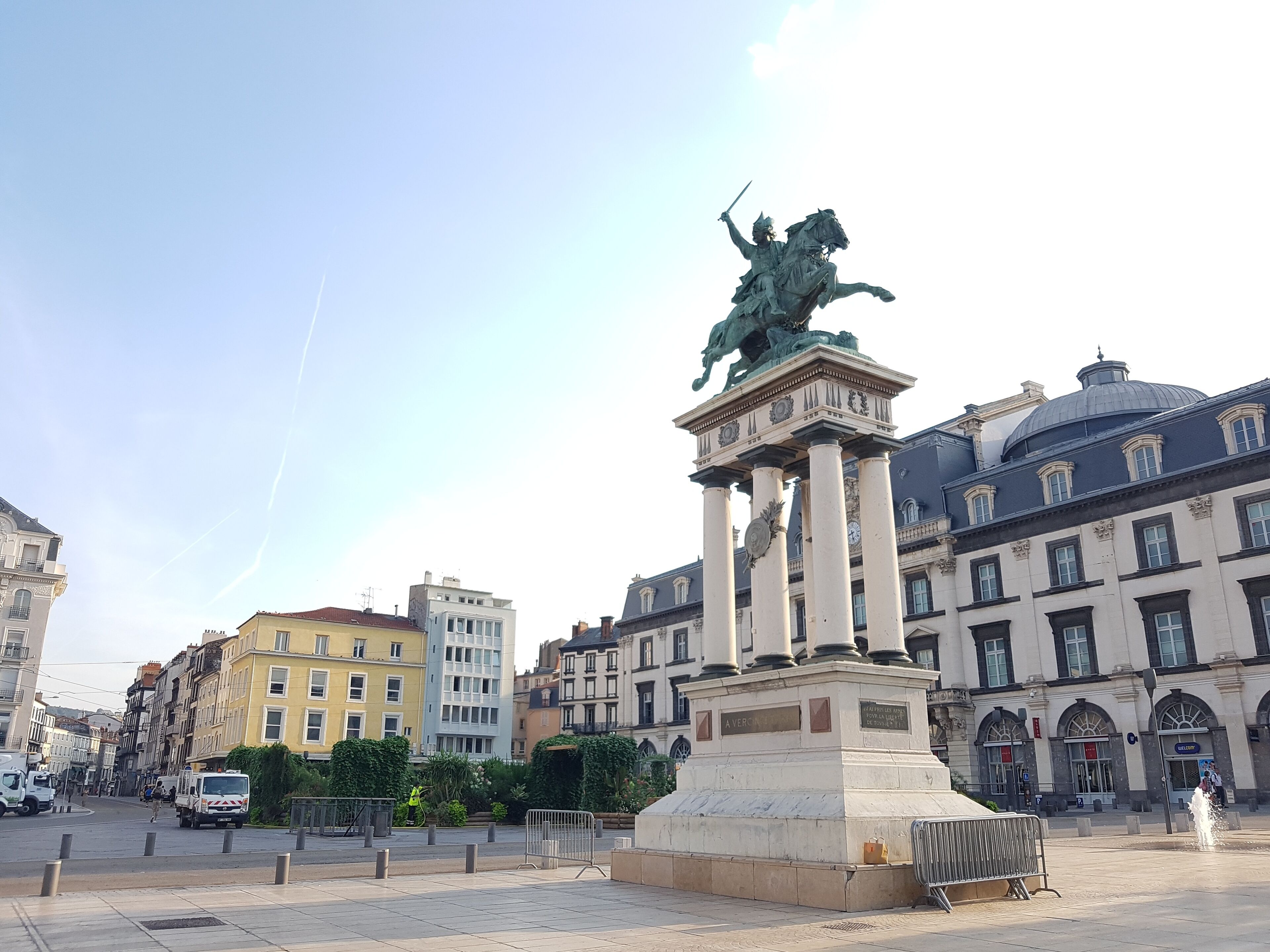 Une statue représentant une figure à cheval, située sur une place bordée de bâtiments historiques.