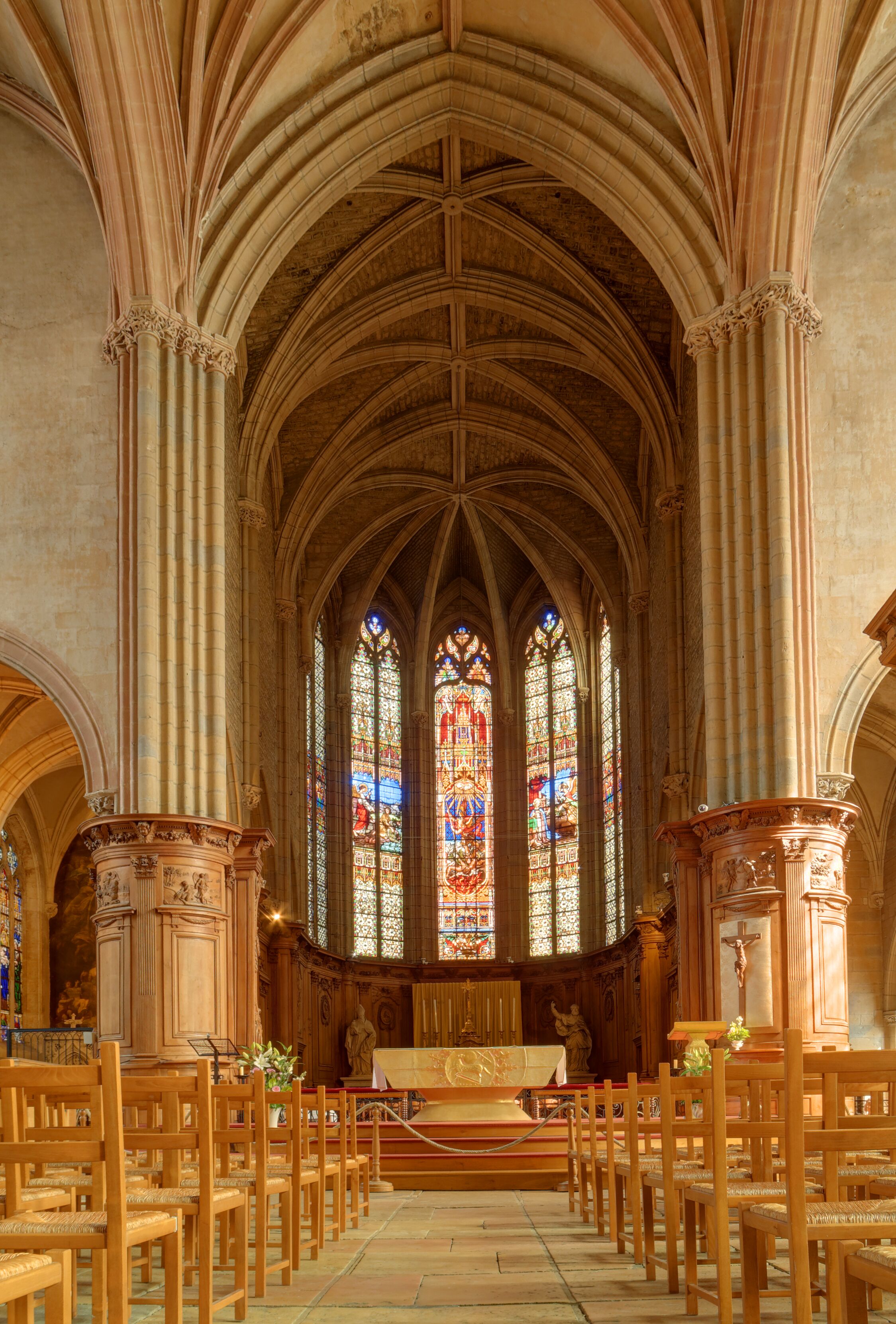 Interior de iglesia con techos abovedados, vidrieras de colores, bancos de madera y un altar central.