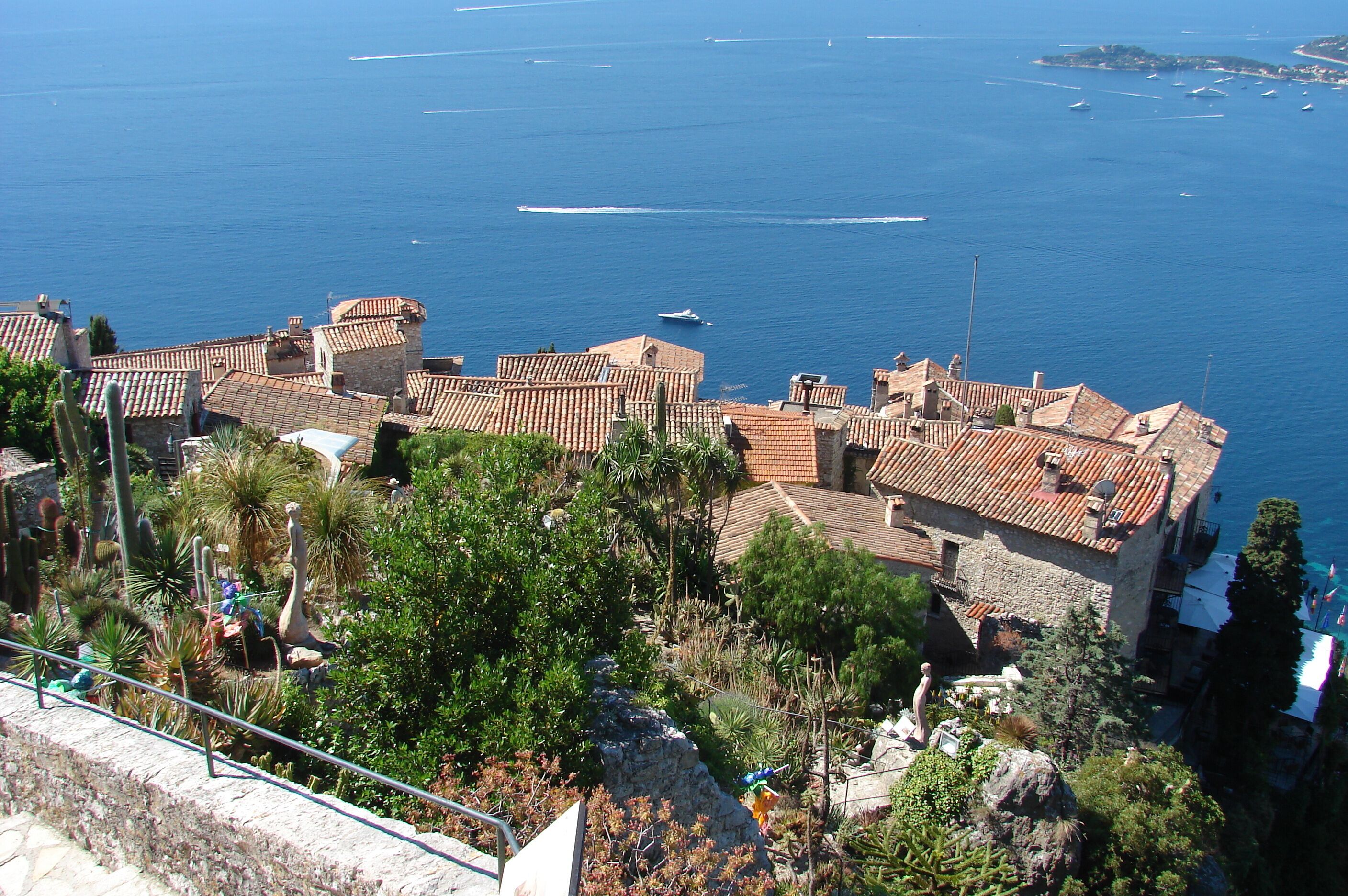 Una cittadina costiera con edifici dalle tegole color terracotta, un mare cristallino e barche.