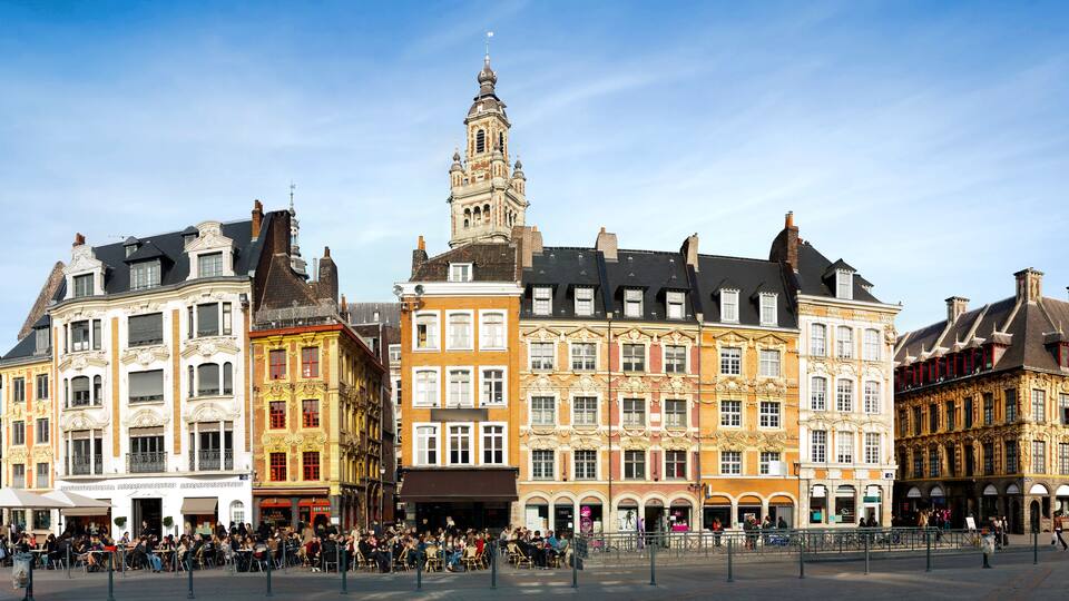 Ein historischer europäischer Platz mit kunstvollen Gebäuden, einem markanten Turm und einer lebhaften Menschenmenge.