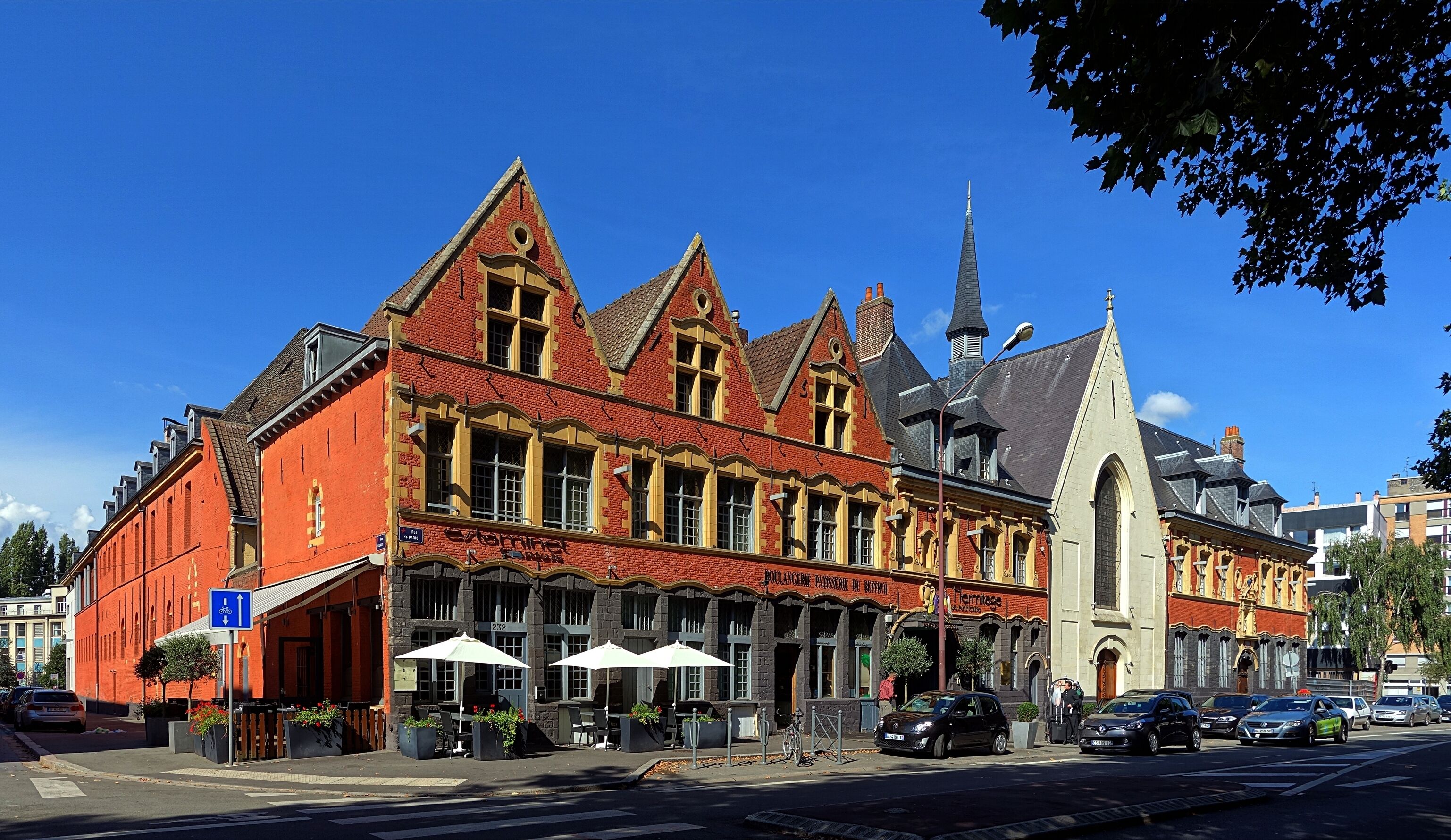 Un bâtiment en briques rouges, surmonté d’un clocher d’église et doté d’une terrasse.