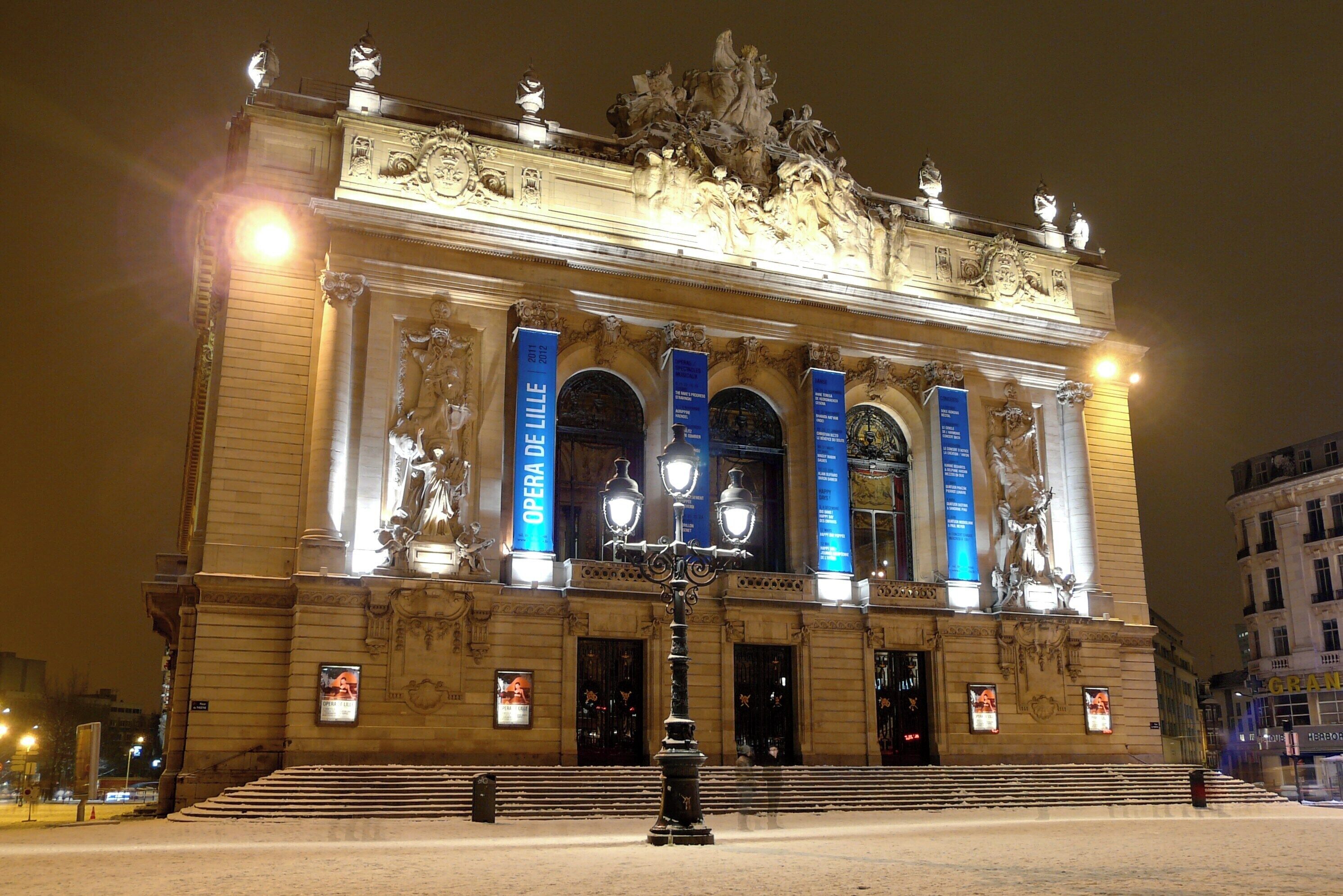 Un majestuoso teatro de ópera con esculturas ornamentadas y banderines azules iluminados.