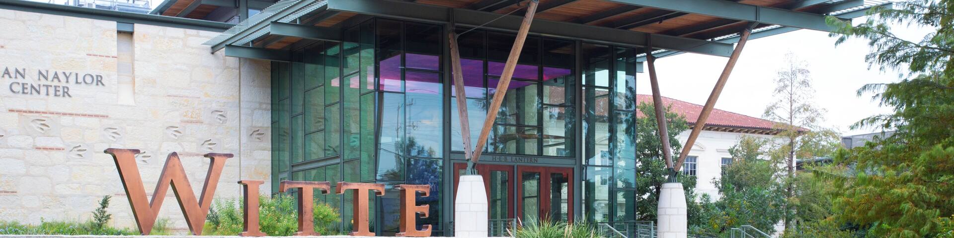 A building with large letters spelling "Witte Museum" and a stone wall with "An Naylor Center" text.
