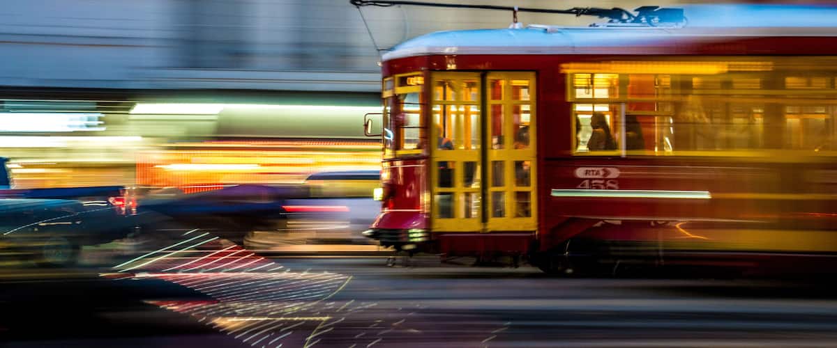 Un tramway rouge agrémenté de touches jaunes, portant l’inscription « RTA 458 » sur son flanc, se déplace dans une rue de la ville.
