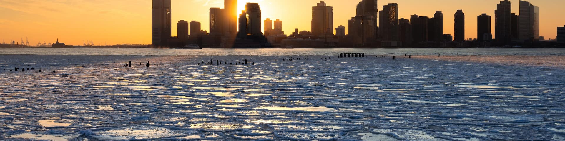 A frozen lake with a city skyline in the background during sunset.