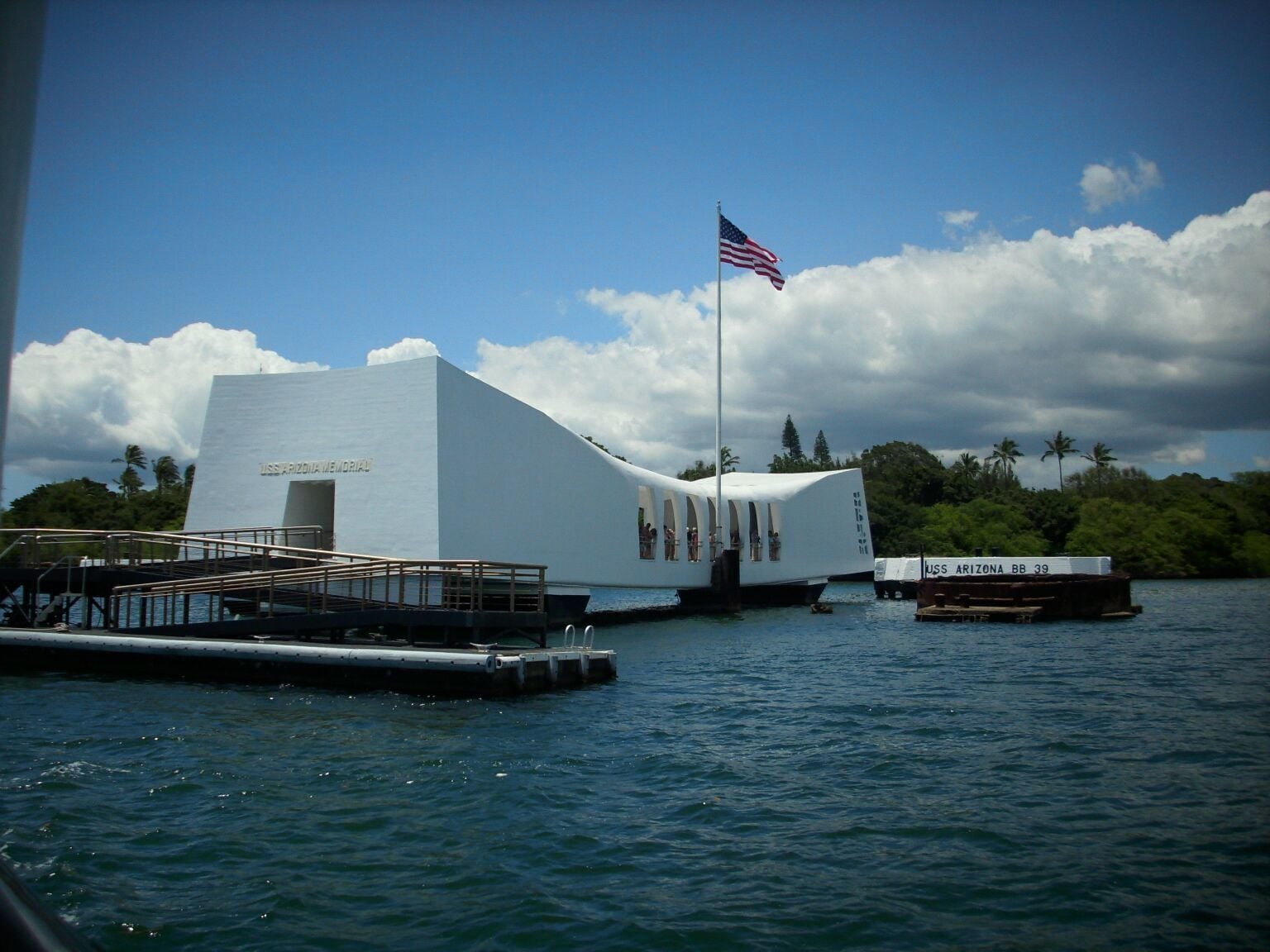 A white building with an American flag, surrounded by water and palm trees.