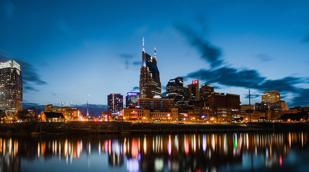 A city skyline at night with a prominent bridge and skyscrapers reflecting on the water.