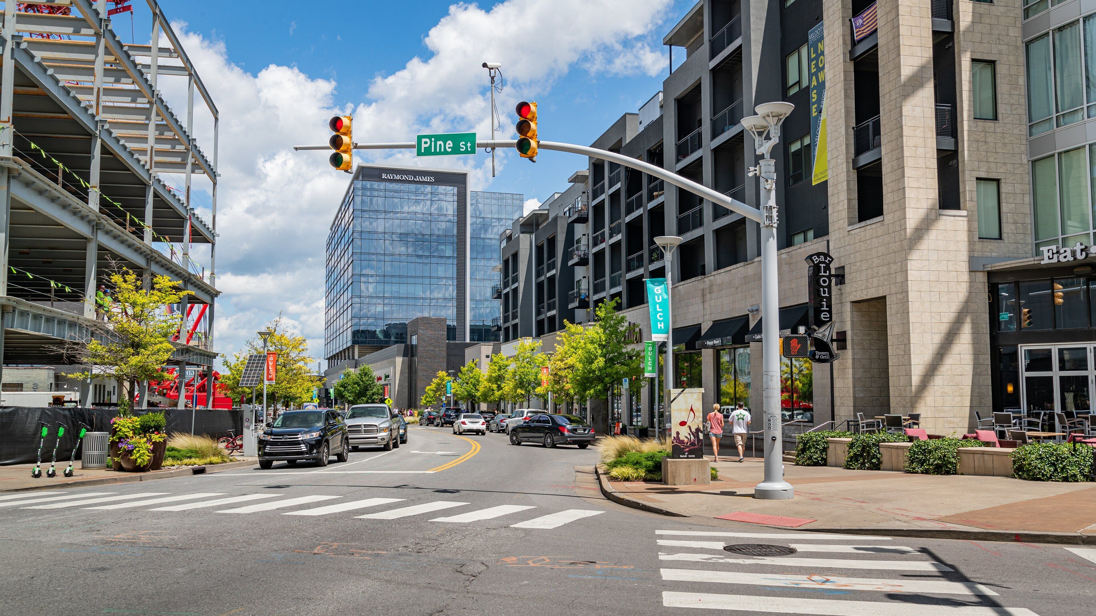 A busy urban street with a crosswalk, traffic lights, and various buildings including a glass skyscraper.