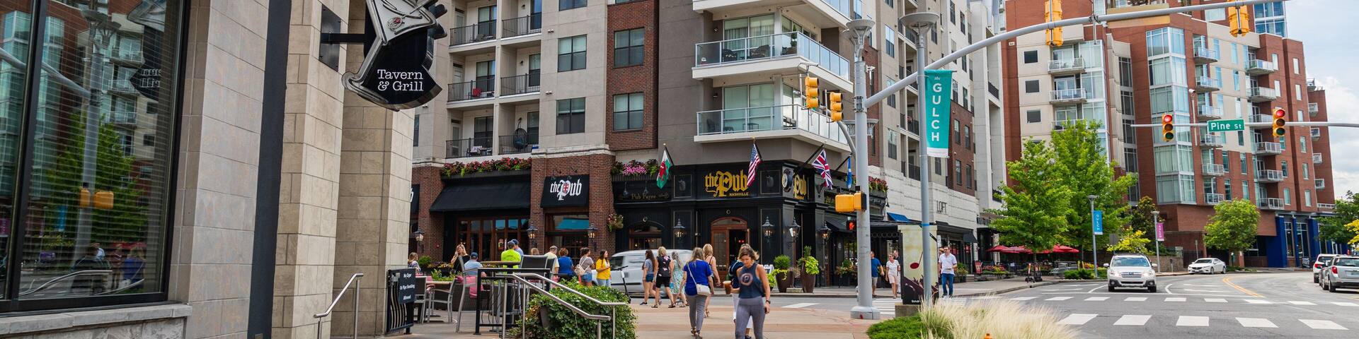 A city street with a bar named "Late Night Dining" and "Bar Louie" on the left. There are multiple buildings, including a modern high-rise and a brick building with balconies.