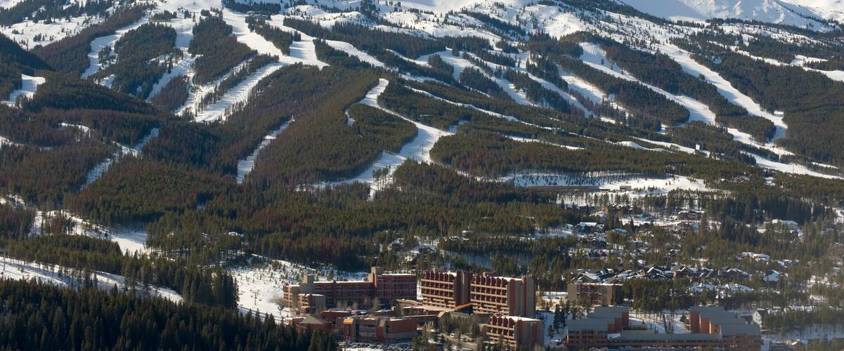Una muntanya coberta de neu amb pistes d'esquí, un poble amb edificis i un cel serè.