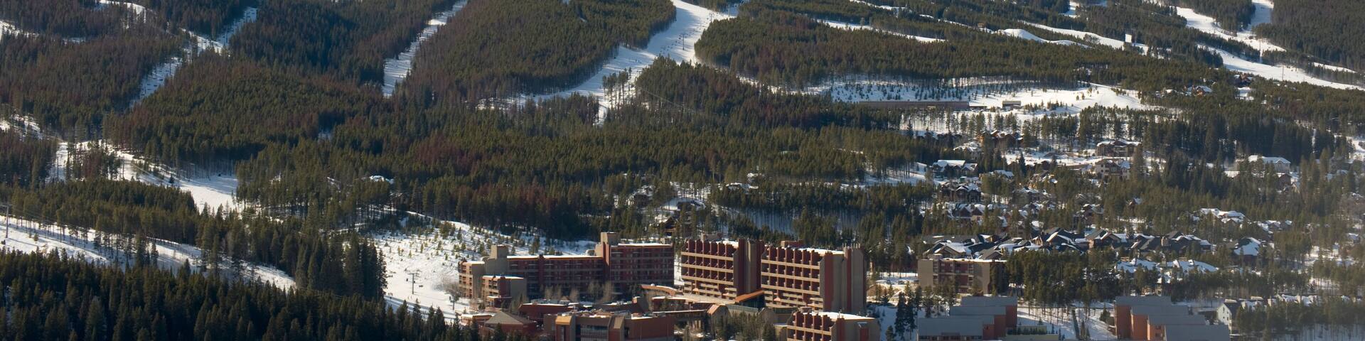A snow-covered mountain with ski trails, a town with buildings, and a clear sky.