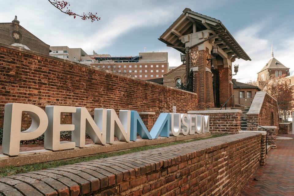 Het Penn Museum bord met een bakstenen muur en gebouwen op de achtergrond.