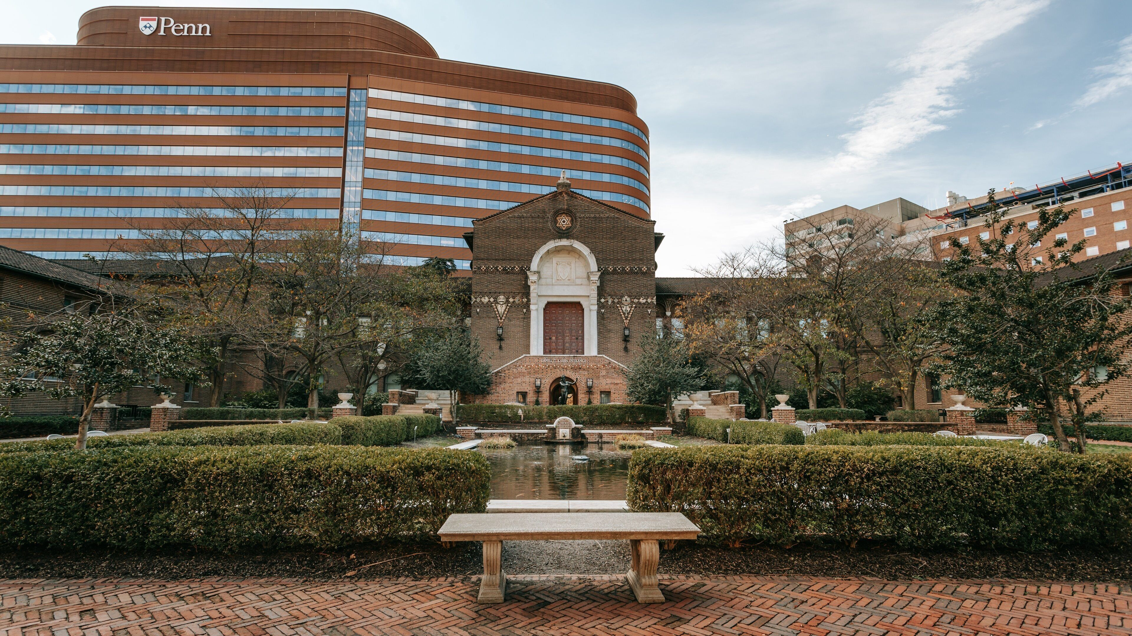 A courtyard with a fountain, a bench, and a building with a Penn logo.